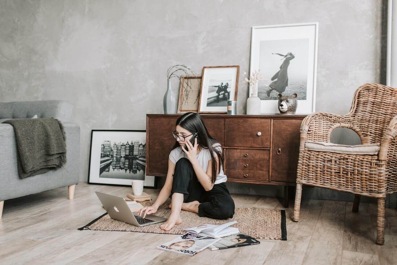 Woman sitting on the floor looking at a laptop while talking on the phone