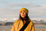 Woman wearing yellow beanie and yellow jacket near snowy mountains